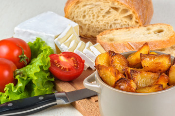 Breakfast from bread, cheese, tomatoes, potatoes and all-over salad on a wooden table closeup.