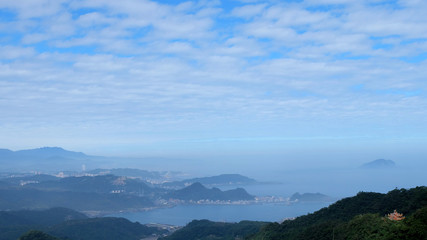 Fototapeta na wymiar Scenery from the Jilong Mountain, Taiwan, with cloudy blue sky, mountain, sea, and a small temple in the bottom right corner.