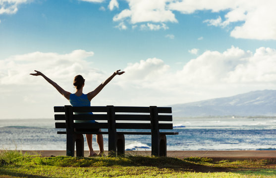 Happy woman sitting on park bench enjoying the beautiful ocean view. 