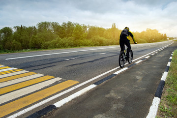 The cyclist is moving along the motorway.
A horizontal. A figure of a man on a bicycle moving into the distance in perspective from the left to the right along  with yellow and white markings