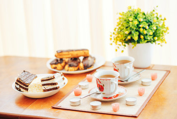 Sweet cakes with two cups of tea on a wooden table.