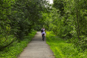 back view of Young woman rides a bike along in a park