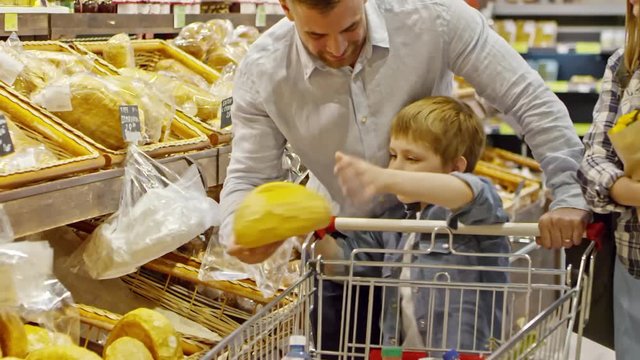 Slowmo of mother, father and little son walking with shopping cart and choosing fresh bread in supermarket