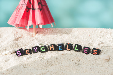 Word Seychelles is made of multicolored letters on snow-white sand against the blue sea. Tourism, rest, resort, sea, sun, beach
