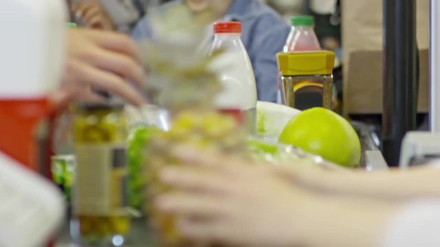 Tilt up slow motion shot of smiling young mom, son and dad putting groceries on conveyor belt at register in supermarket while cashier scanning products