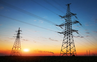 Silhouette of electricity pylons and high-voltage power lines on the field at sunset. Wire...