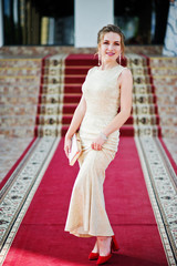 Portrait of a stunning young woman in pretty evening gown posing on the carpet indoors.