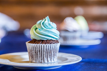 Tasty cupcake with blue butter cream on the white plate.