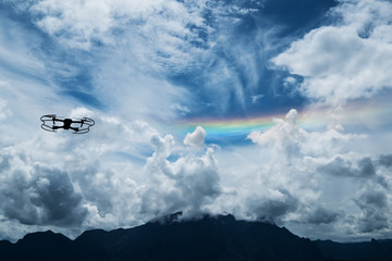 Silhouette drone flying on blue sky with rainbow