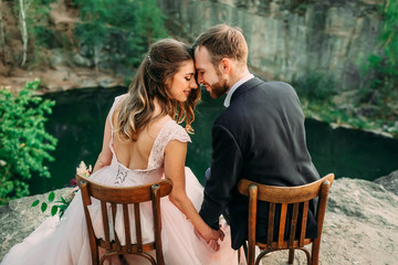 Newlyweds sitting at the edge of the canyon and couple looking each other with tenderness and love. Bride and groom touching foreheads. Wedding