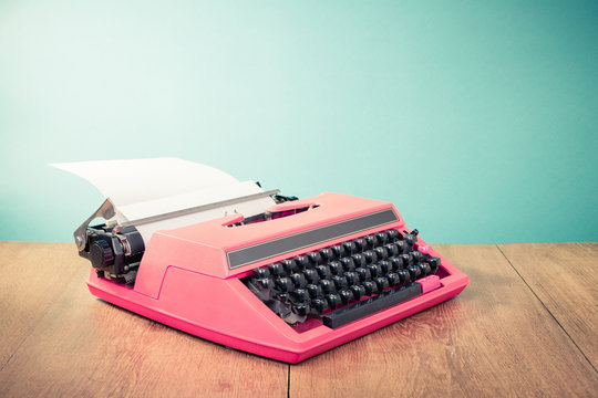 Retro pink typewriter with paper on wooden table front mint green background. Vintage old style filtered photo
