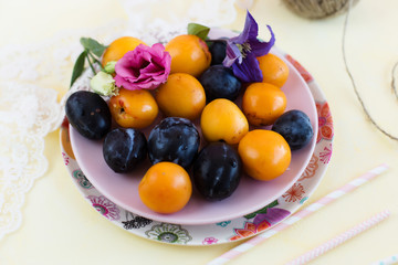 Plums and apricots on the plate on yellow background