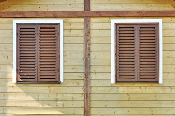 Wall of the wooden building with two window and closed brown shutters.