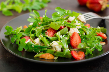 Salad with arugula, strawberries, cottage cheese, olive oil, on a black plate, Old black background. Close-up. Top view