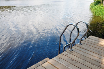 Wooden pier with metal railing on background of the river.