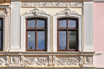 Two wooden windows with white decorative elements on facade. Grodno, Belarus.