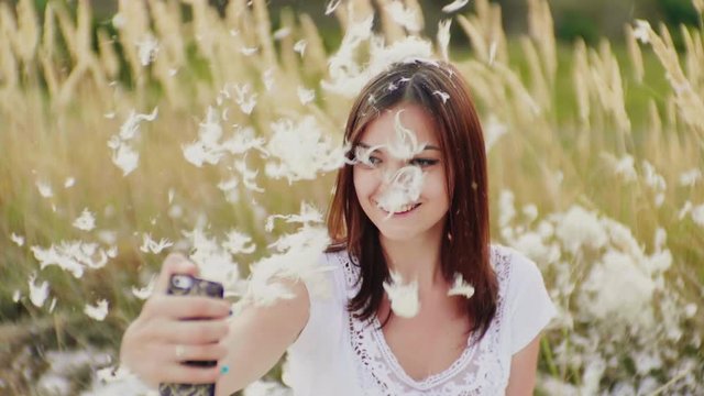 A woman makes selfie on a creative photo shoot. Everything is strewn with feathers.