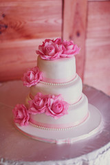 Obraz na płótnie Canvas Wedding cake covered with white icing and decorated with pink roses