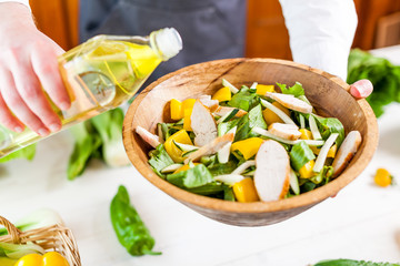 man pouring olive oil into healthy chicken salad on kitchen