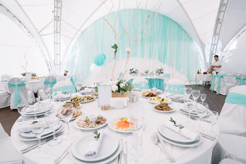 White tables decorated with mint cloth stand under the tent
