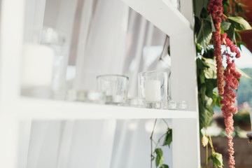 Little white candles stand on a white shelf