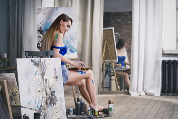 Young female artist painting abstract picture in studio, beautiful sexy woman portrait