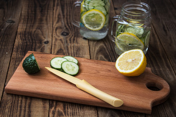 Cucumber and lemon slices on a cutting board and a jar on the background