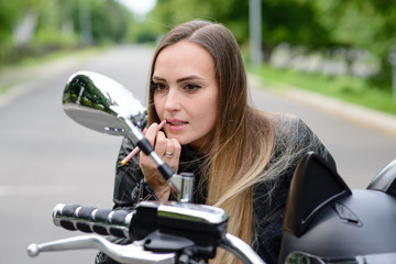 Fototapeta na wymiar Biker girl paints her lips on a motorcycle.