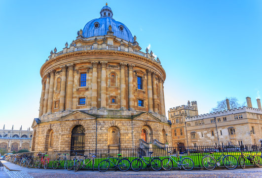 OXFORD, ENGLAND - DECEMBER 6, 2014: Bicycles chained against railings in front of Radcliffe Camera by cobbled street in Oxford University, There is the main teaching and research science library