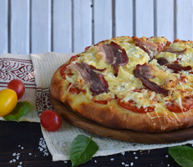 Homemade delicious pizza with cheese, tomato and prosciutto ham on a dark wooden background.