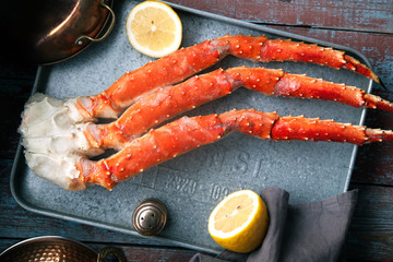 Fresh crab claws on metallic tray on vintage wooden background with copper plates and lemon slices.