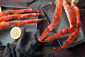 Fresh crab claws on metallic tray on vintage wooden background with copper plates and lemon slices.