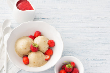 Vegan banana ice cream with strawberry sauce and fresh strawberries in a white bowl on a light blue wooden background