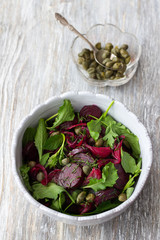 Beetroot salad with baked red onion, capers, watercress, greens and vinaigrette sauce. Vegan healthy food. In a blue bowl on a wooden table