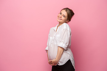 Young beautiful pregnant woman standing on pink background