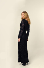 Fototapeta premium full length portrait of a blonde lady wearing black lace dress, standing pose, isolated against creamy studio background.