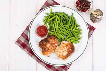 Lunch from green beans and cutlets on white wooden table