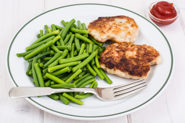 Lunch from green beans and cutlets on white wooden table