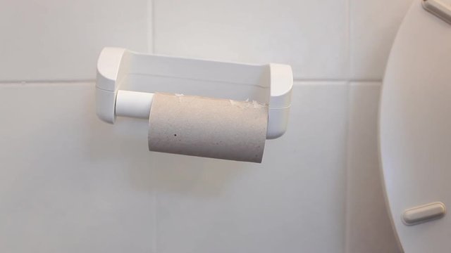 A man sitting on the toilet, having to deal with a hard problem: an empty paper roll. Front close-up shot.
