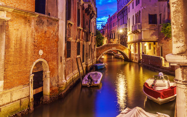 Fototapeta na wymiar Venice at night with boats on canals, lights and typical Venetian buildings.