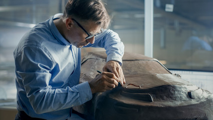 Senior Automotive Designer with Rake Sculpts Futuristic  Car Model from Plasticine Clay. He Works in a Special Studio Located In a Large Car Factory.