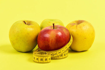 Tape for measuring and four apples, isolated on yellow background