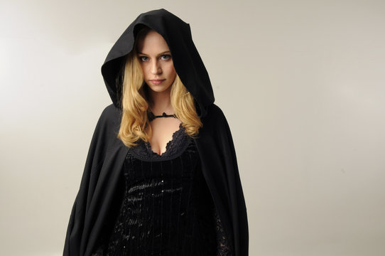 portrait a pretty blonder wearing black hooded cloak. soft cream background