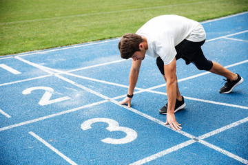 Young man standing in starting position for running on track