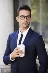 Serious businessman holding coffee and looking away