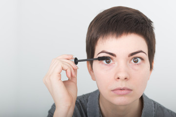 Young beautiful woman applying mascara on eyes. Beauty make-up. Portrait of girl with fake eyelashes applying black mascara holding brush in hand. Sexy female with soft skin and perfect makeup.