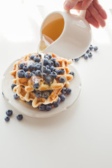 cropped shot of woman pouring syrup from saucer on tasty waffles