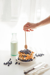 cropped shot of woman pouring honey from spoon on tasty waffles