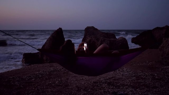 Young Girl Using Mobile Phone In Hammock At The Beach At Night. HD Slowmotion. 1920x1080