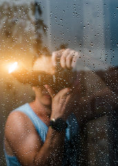 A man is standing behind a glass, and on the glass a drop of rain